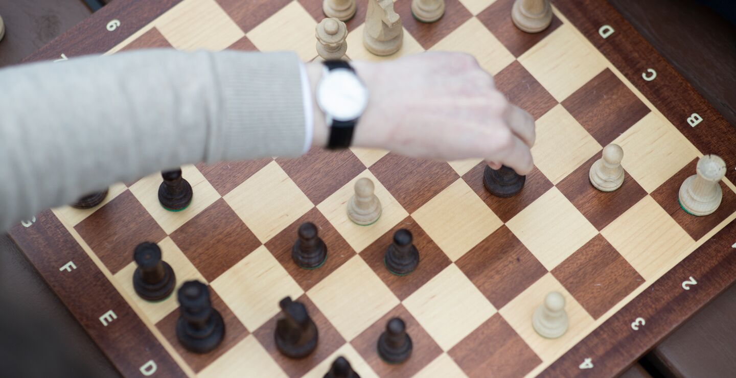 En hånd som tar tak i en brikke på et sjakkbrett